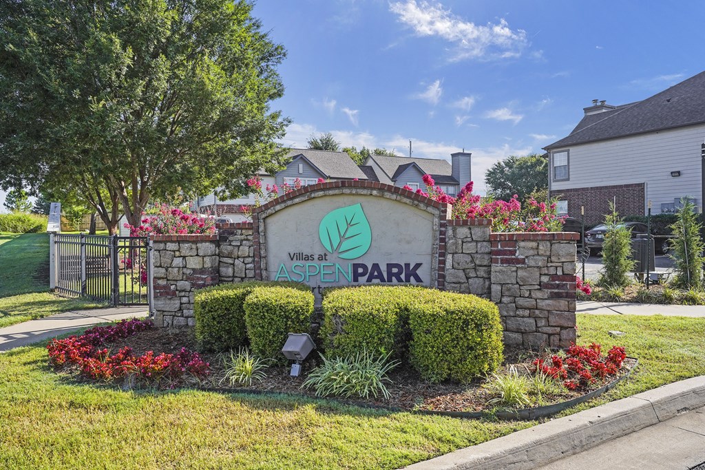 A sign for Villas at Aspen Park is surrounded by flowers and greenery.