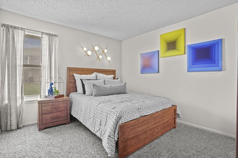 A bedroom with a bed, nightstand, and three colorful paintings on the wall.
