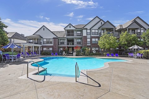 A large swimming pool surrounded by a fence and chairs in front of apartment buildings.