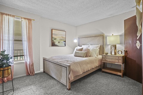 A bedroom with a large bed and a small table with a plant on it.