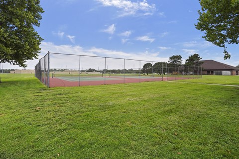 A tennis court is enclosed by a fence and surrounded by a grassy area.