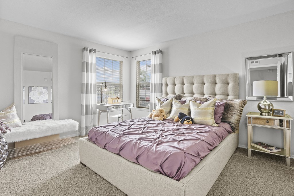 A bedroom with a bed covered in a purple comforter and a white headboard.