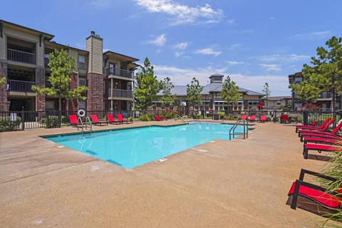 A swimming pool surrounded by red chairs and apartment buildings.