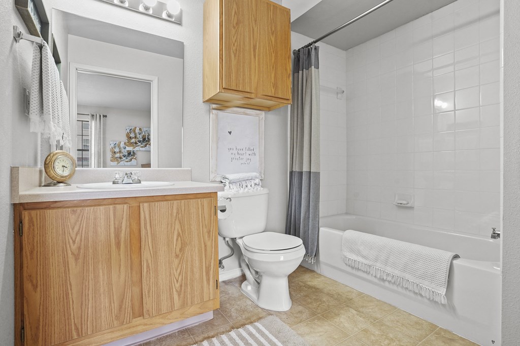 A white toilet sits in a bathroom with a wooden cabinet and a white bathtub.
