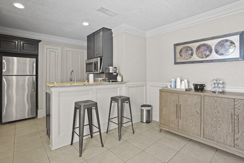 A kitchen with a refrigerator, bar stools, and a cabinet.