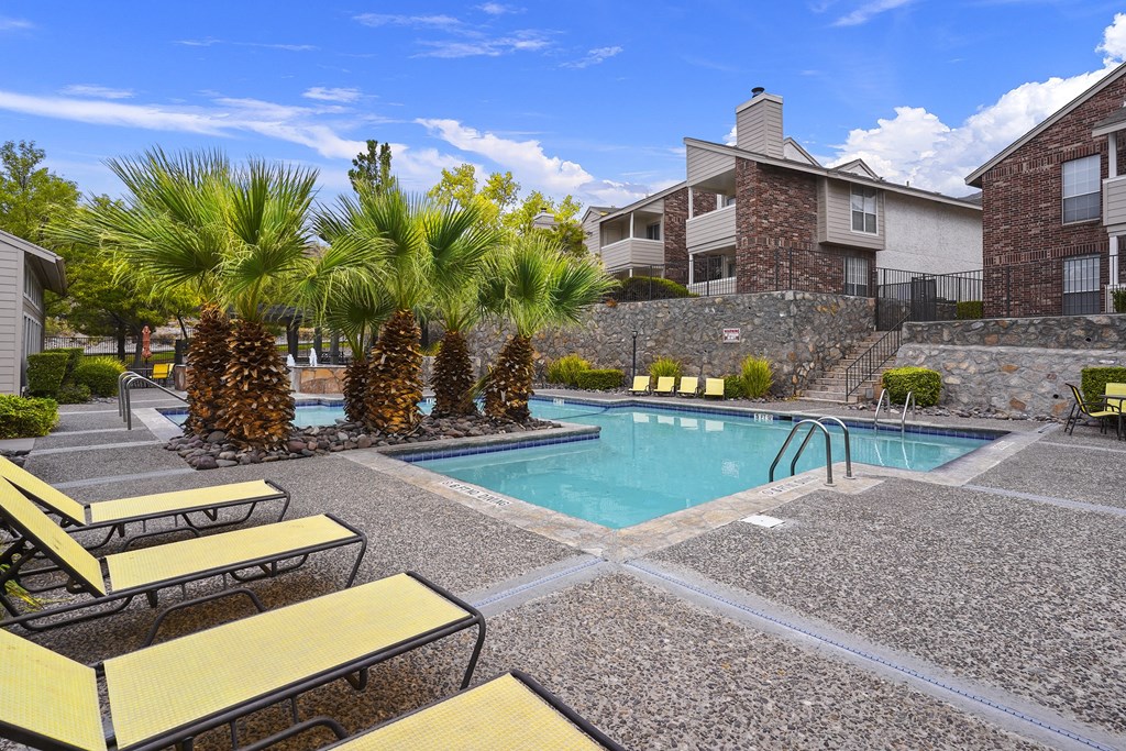 A pool surrounded by yellow sun loungers and palm trees.