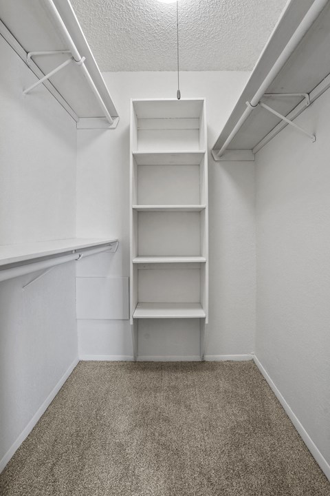 A white shelving unit with four shelves is in a white room with carpeted floor.