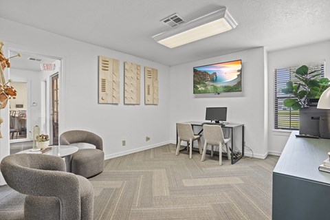 A room with a desk, chairs, and a painting on the wall.