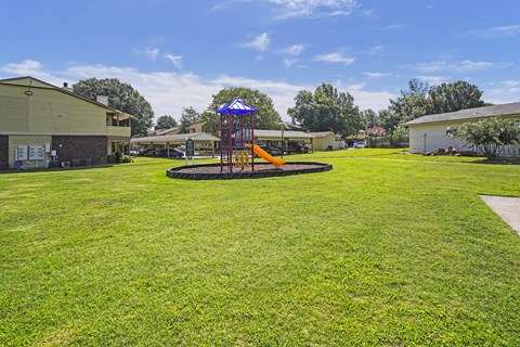 A playground with a swing set and a blue canopy is in the foreground of a grassy area.