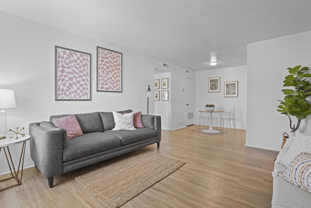 A grey couch with pink pillows is in the middle of a room with a rug on the floor.