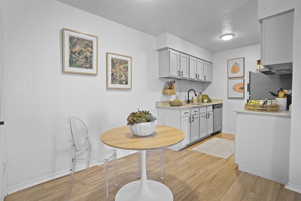 A kitchen with a table and chairs in the foreground and a counter with fruit on it in the background.