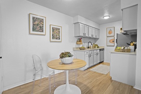 A kitchen with a table and chairs in the foreground and a counter with fruit on it in the background.