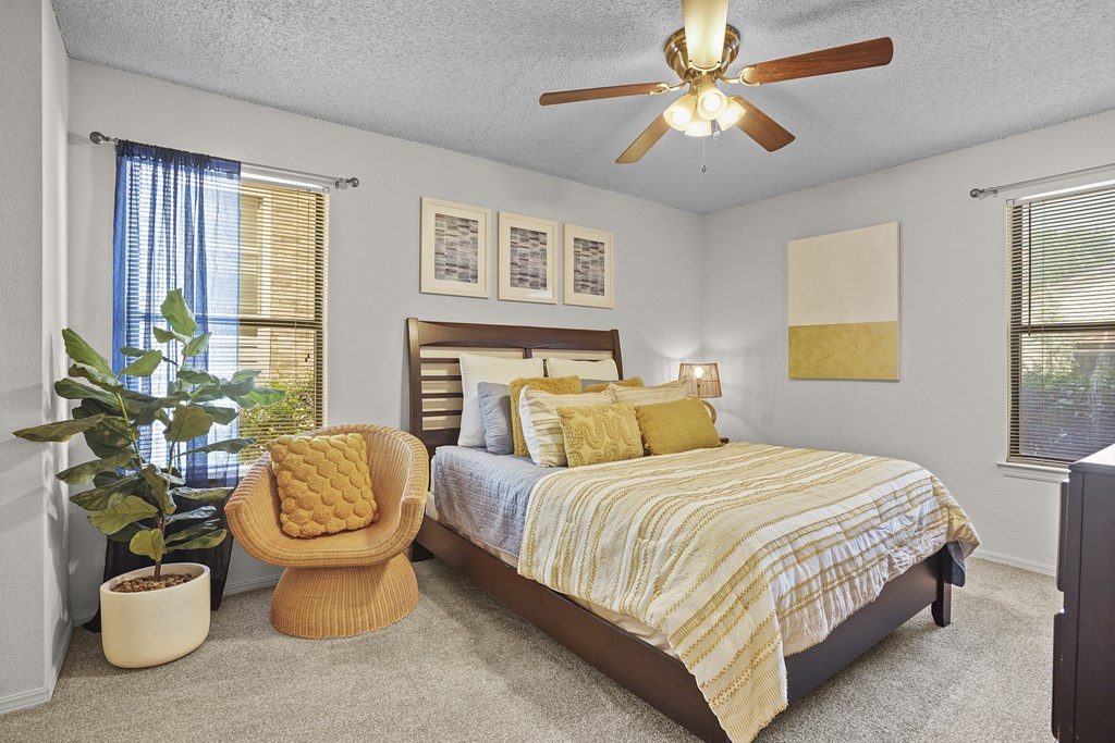 A bedroom with a bed, chair, and potted plant.