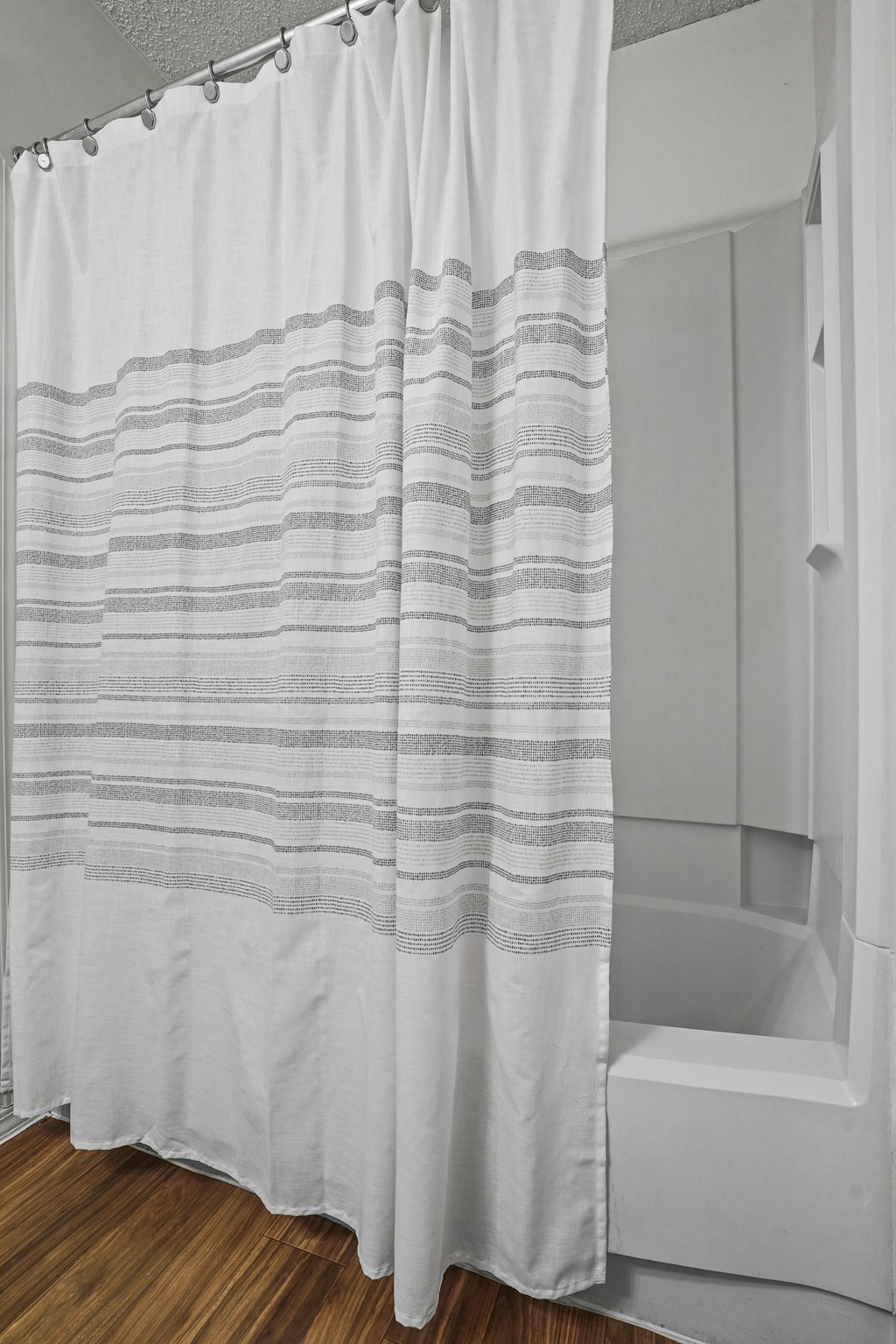A white shower curtain with grey stripes hangs in a bathroom.