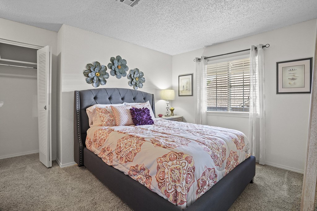 A bedroom with a large bed and a window with blinds.