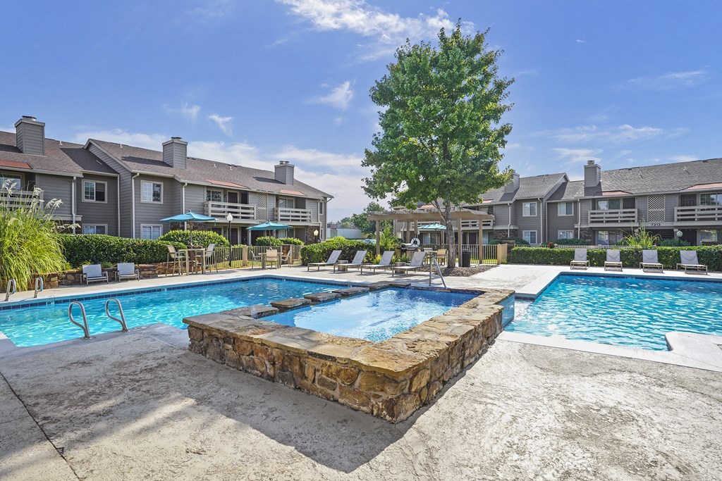 A swimming pool surrounded by a stone wall and chairs.
