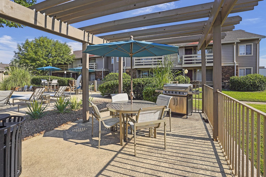 A patio with a table and chairs under a wooden pergola.