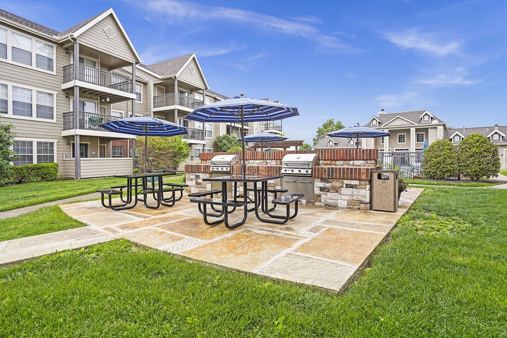 A sunny day at a residential area with apartment buildings, picnic tables, and umbrellas.