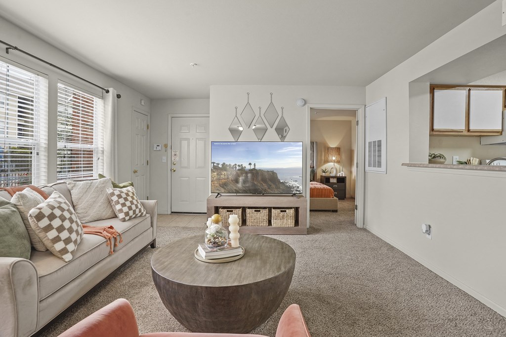 A living room with a couch, coffee table, and a television displaying a beach scene.