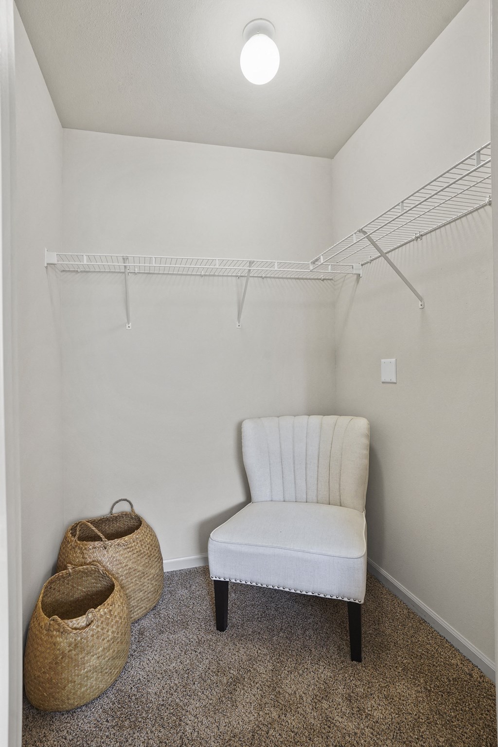 A white chair sits in a corner of a room with a white wall and a white shelf above it.