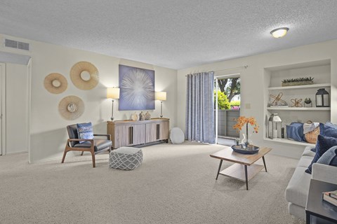 A living room with a grey sofa, a wooden coffee table, and a large window with curtains.