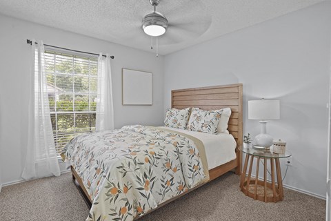 A bedroom with a bed, a ceiling fan, and a small table with a lamp.