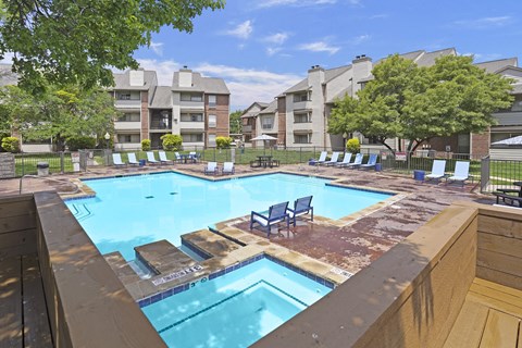 A large swimming pool with lounge chairs and apartment buildings in the background.