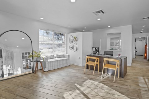 A modern living room with a white couch, a wooden desk, and a large window with blinds.