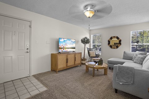 A living room with a grey couch, a wooden cabinet, a flat screen TV and a ceiling fan.