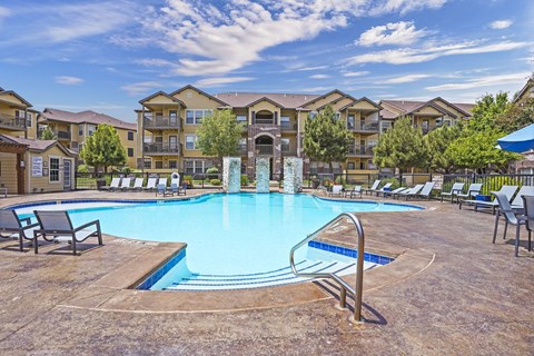 A large swimming pool surrounded by lounge chairs in front of apartment buildings.