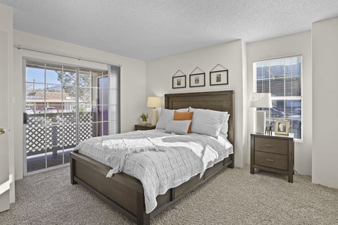 A bedroom with a bed, nightstand, and a window with a view of a parking lot.