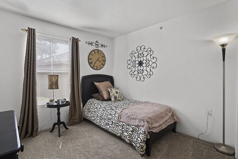 A bedroom with a bed, a clock, a table with a lamp, and a floor lamp.