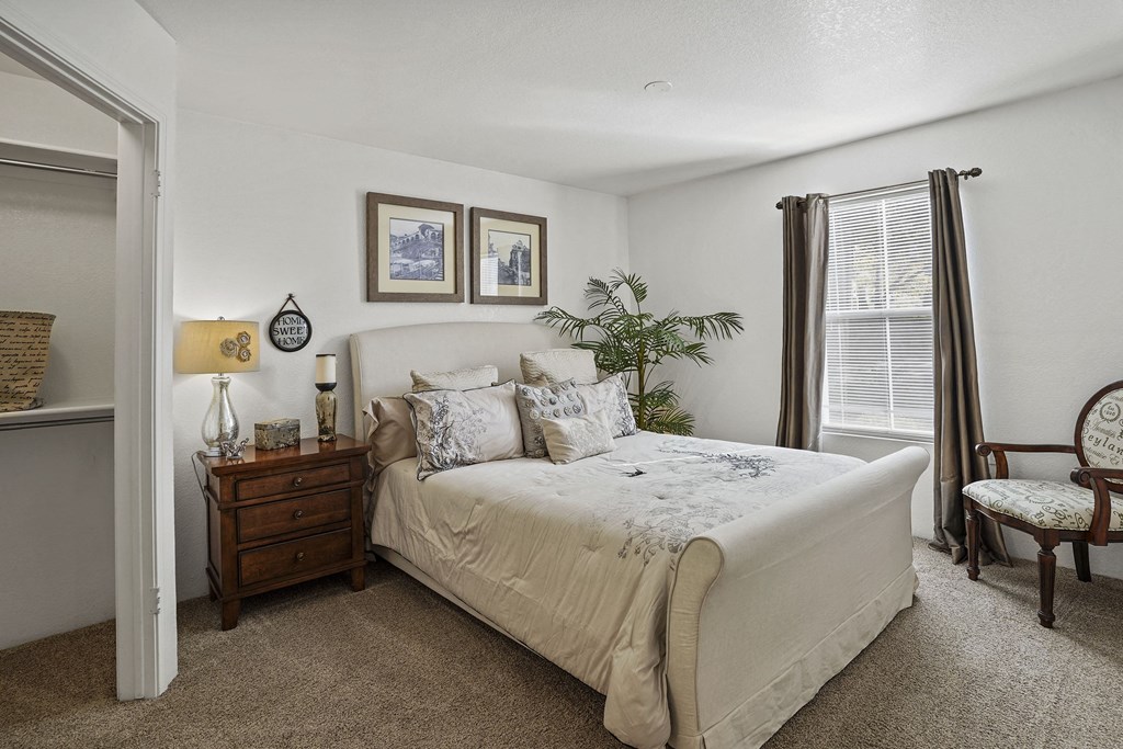 A bedroom with a large bed, a chair, and a nightstand with a lamp.