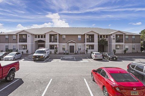 A red car is parked in a parking lot in front of a building.