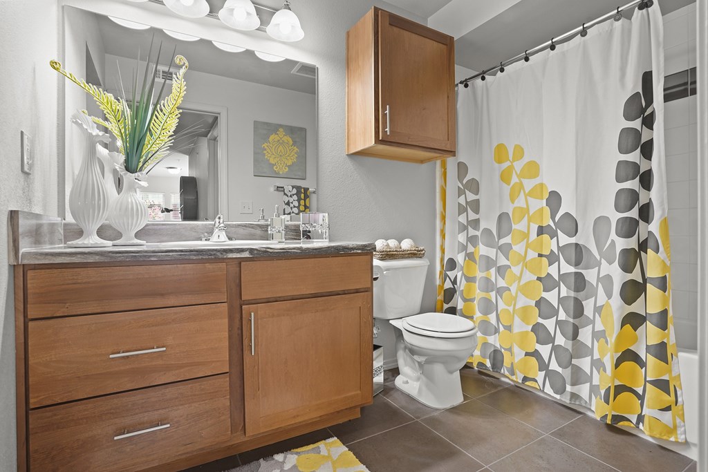 A bathroom with a white toilet and a yellow and grey shower curtain.