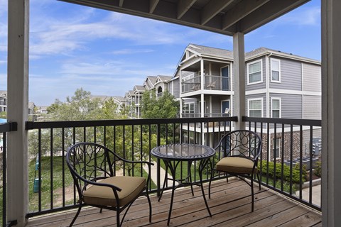 A balcony with a table and two chairs overlooks apartment buildings.