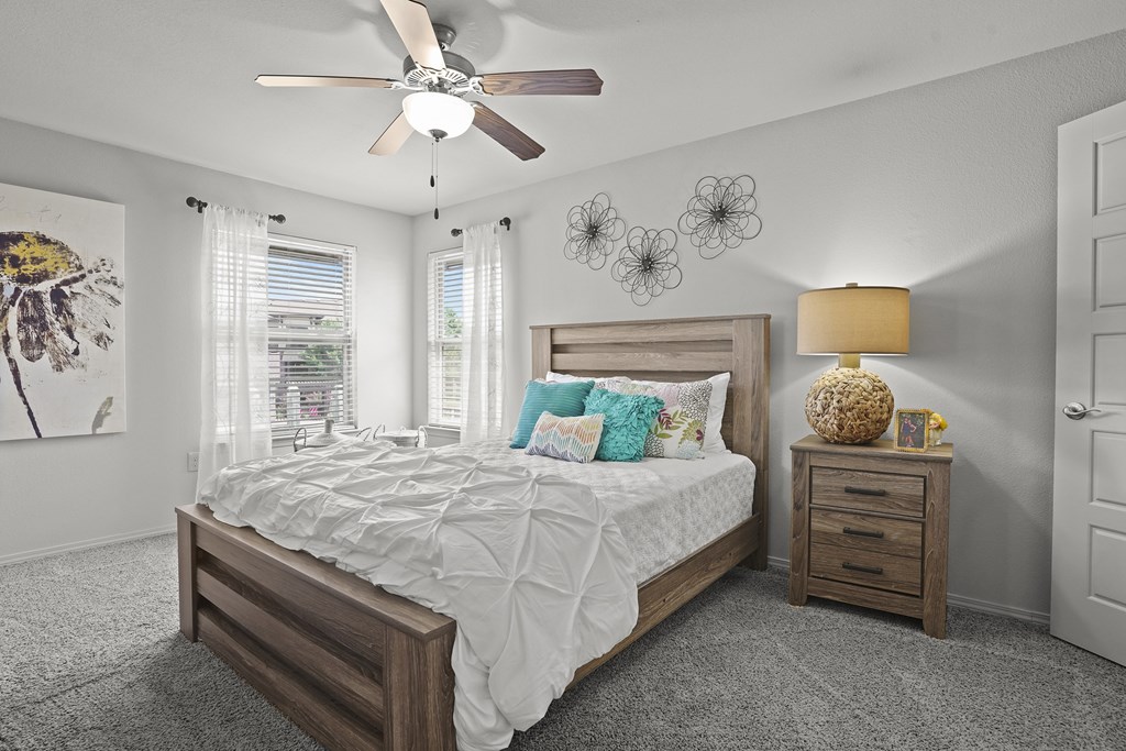 A bedroom with a large bed, a ceiling fan, and a painting on the wall.