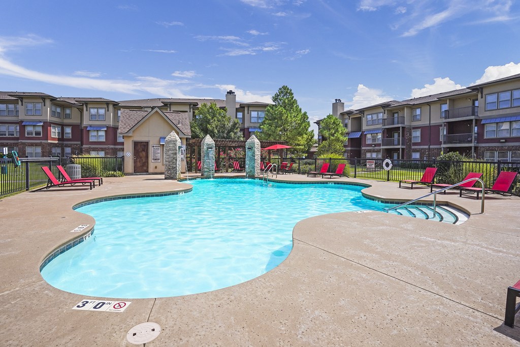 A large swimming pool surrounded by red chairs and apartment buildings.