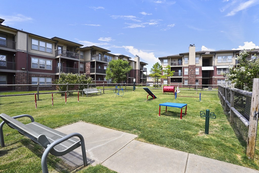 A park with a bench, a playground and apartment buildings in the background.