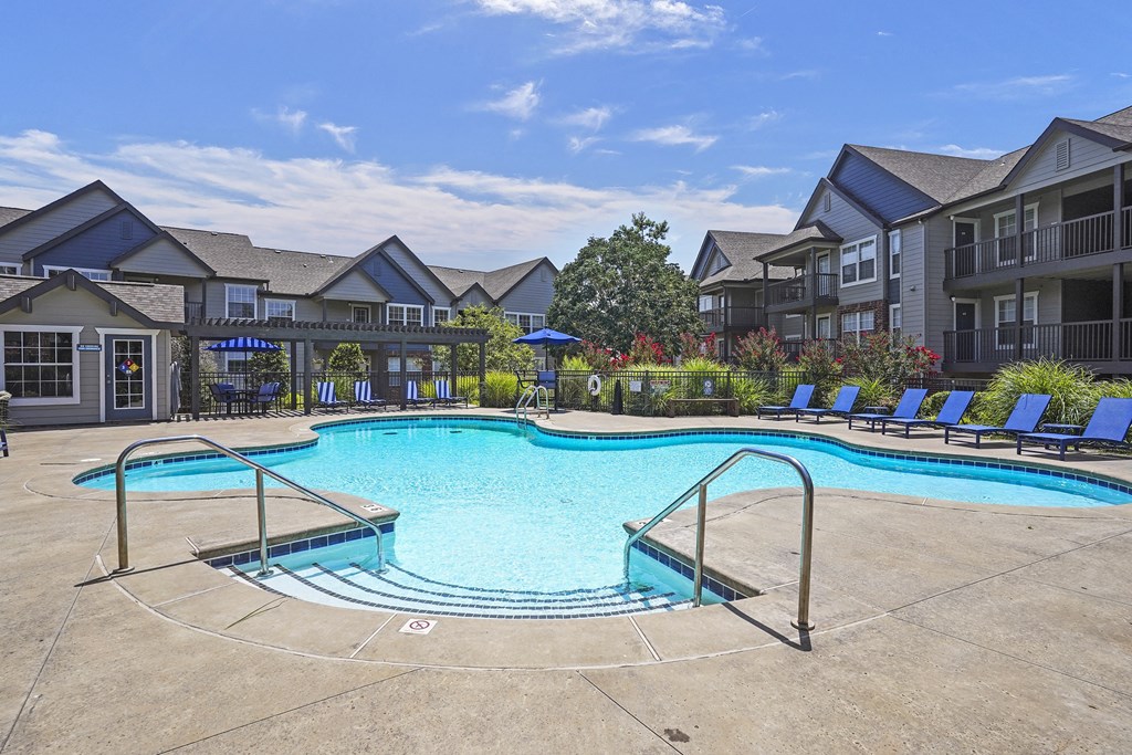 A large swimming pool surrounded by lounge chairs and umbrellas in a residential area.