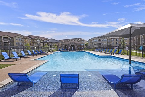 A large swimming pool with blue lounge chairs and a black umbrella.