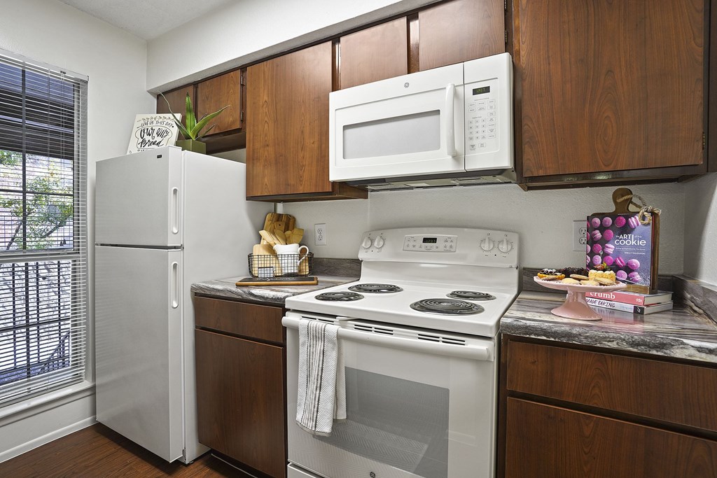 A kitchen with a white refrigerator, white microwave, white oven, and brown cabinets.