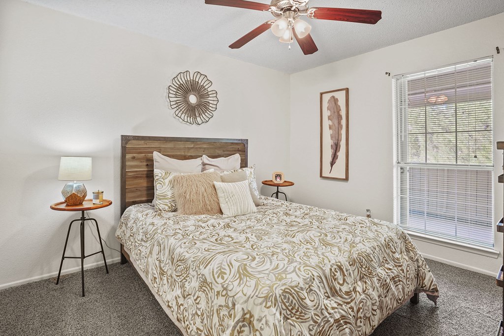 A bedroom with a bed, a ceiling fan, and a window with blinds.
