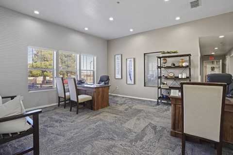 A room with a desk and chairs with a window and a plant on the shelf.