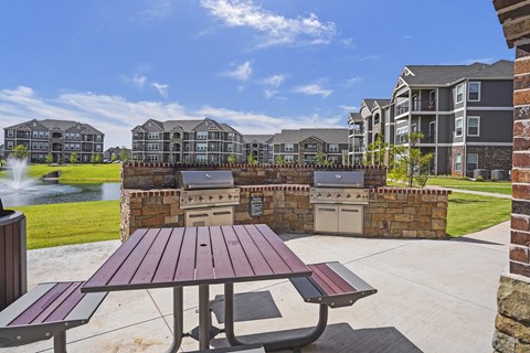 A picnic table sits in the foreground of a sunny courtyard with a fountain and apartment buildings in the background.