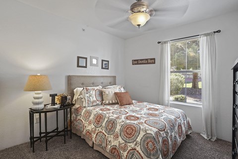 A bedroom with a patterned bedspread and a ceiling fan.