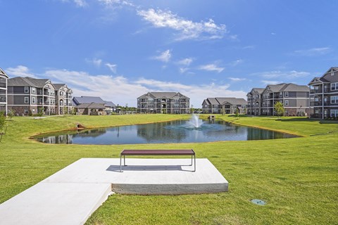 A park with a bench and a pond in front of apartment buildings.