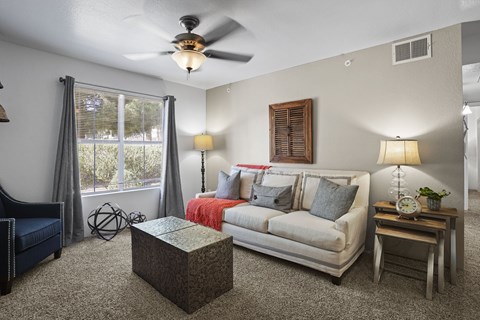 A living room with a couch, a chair, a table, and a ceiling fan.