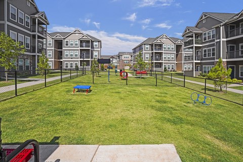 A playground area with a red slide and a blue bench in the middle of a grassy area surrounded by apartment buildings.