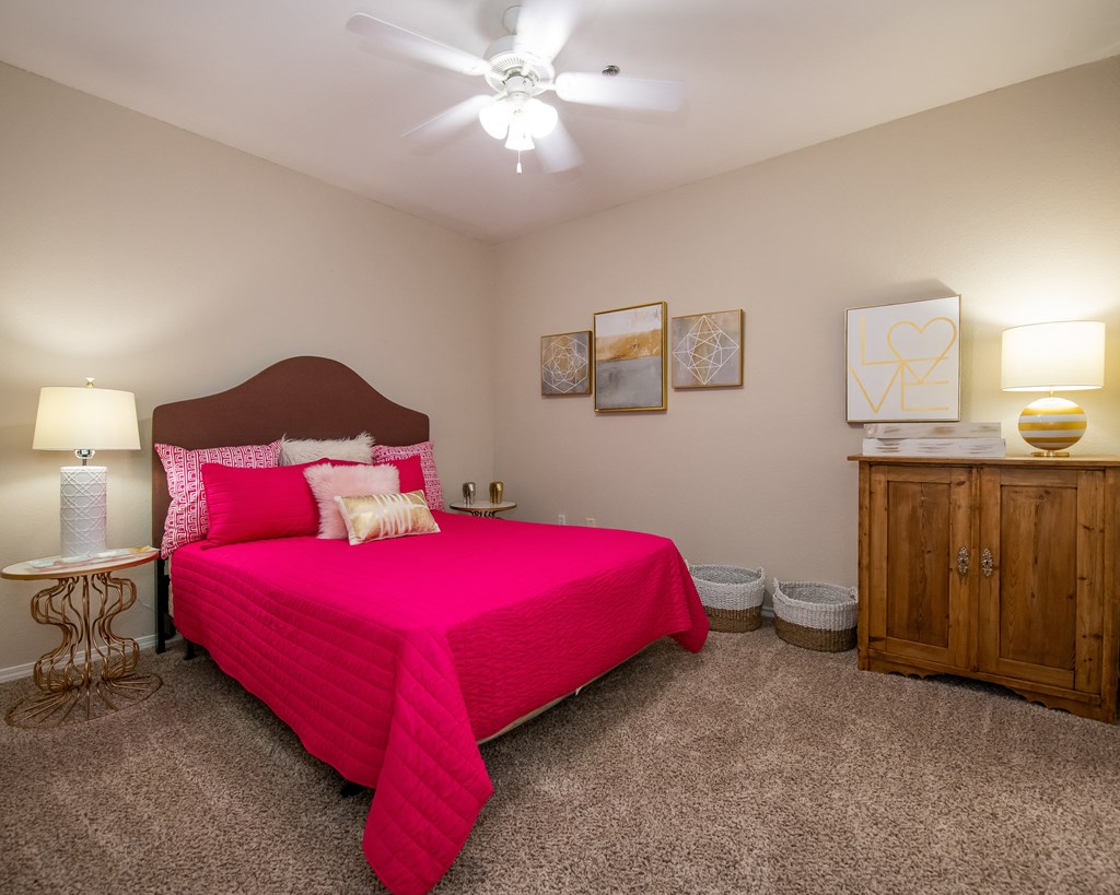 A bedroom with a pink bedspread and a ceiling fan.